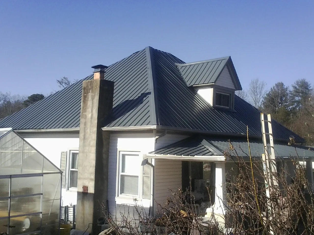 Dark blue standing seam metal roof on a white farmhouse with dormer — Slate & Tile Roof Repair by Roofing Brothers in Ashton
