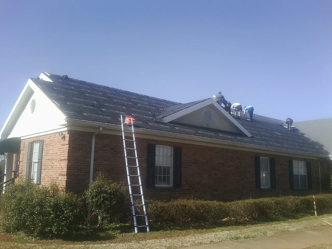 Crew tearing shingles off a brick ranch roof with a ladder set — Emergency Roof Repair work by our crew in Ashton