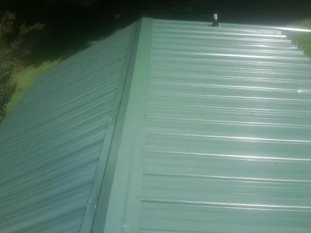 New green metal panels meeting at the ridge of a roof — Flat Roof Repair work by our crew in Ashton