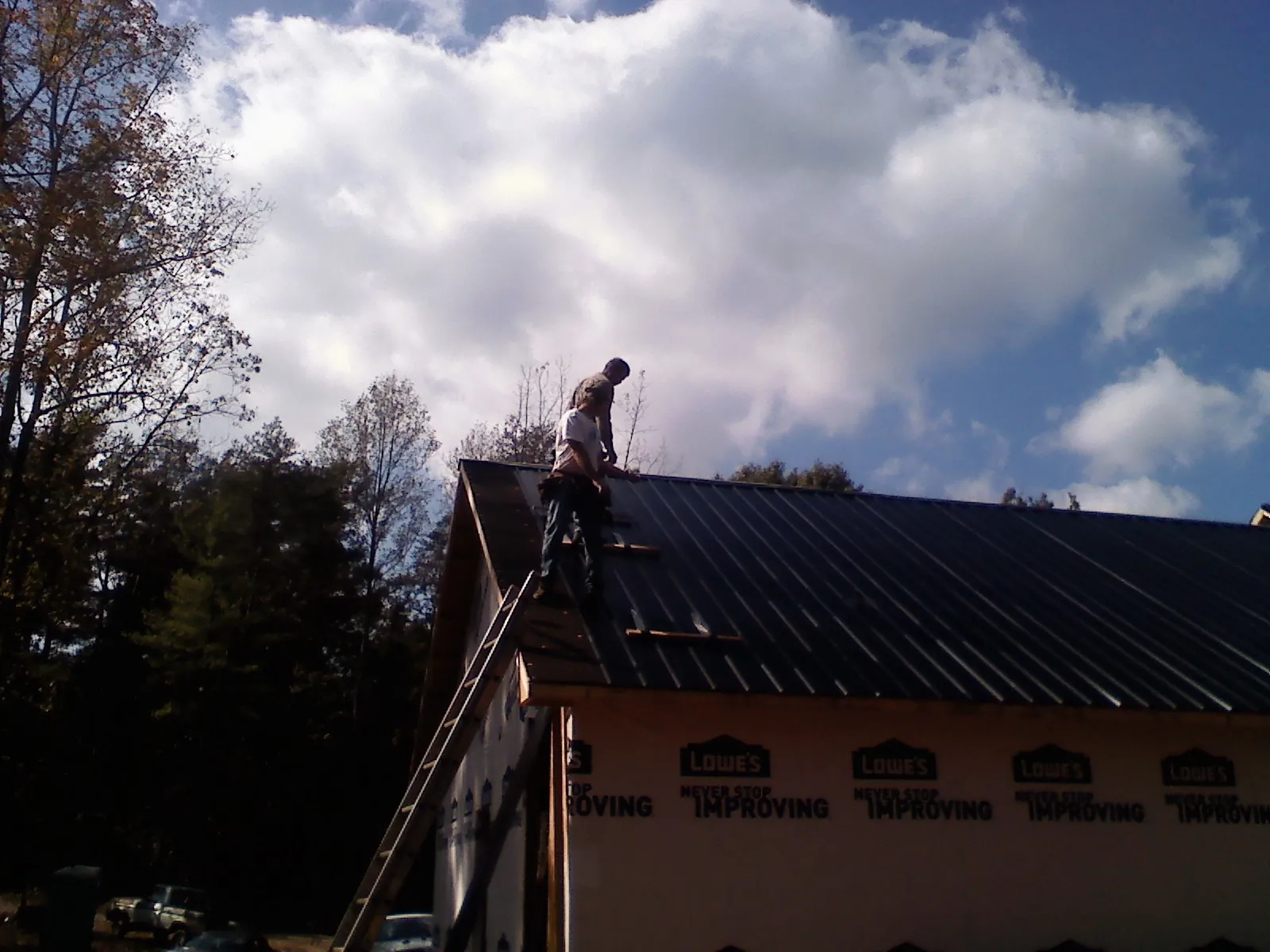 Roofer fastening dark metal panels high against a cloudy sky, from a Roof Inspection job in Ashton
